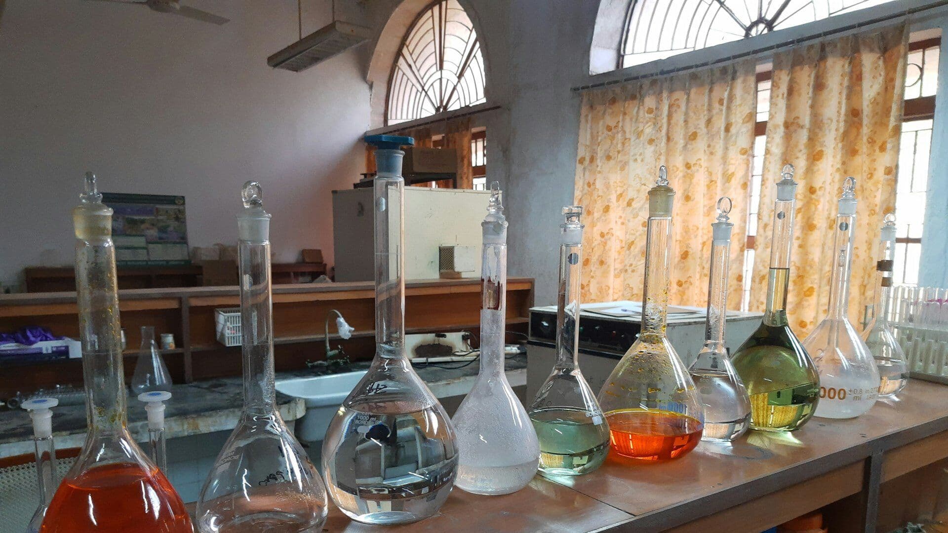 Volumetric flasks of coloured chemical solutions on a laboratory bench