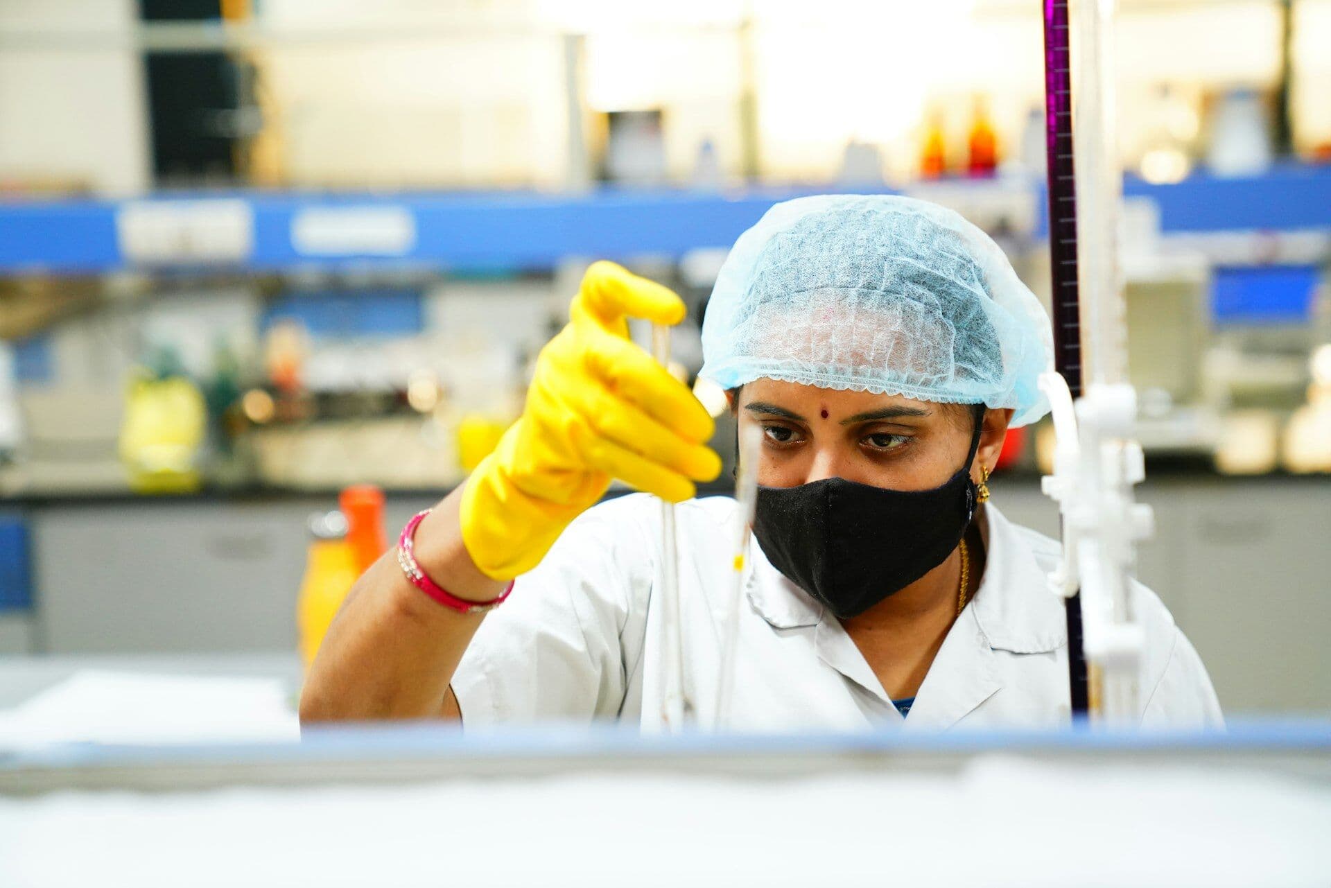 A lab technician in a hairnet and yellow gloves checking a sample