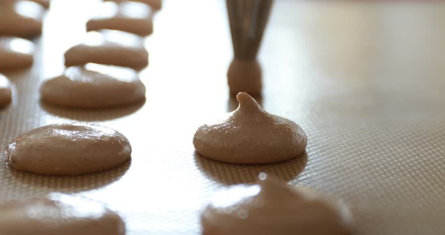 Macaroon batter being piped onto a baking sheet